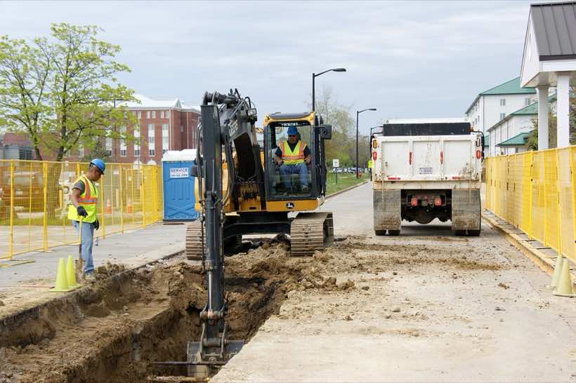 Workers in a trench guiding a large section of new water main into place.
